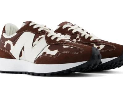 Pair of brown and white cow-print New Balance sneakers with white laces, oversized logos and black lugged soles on white