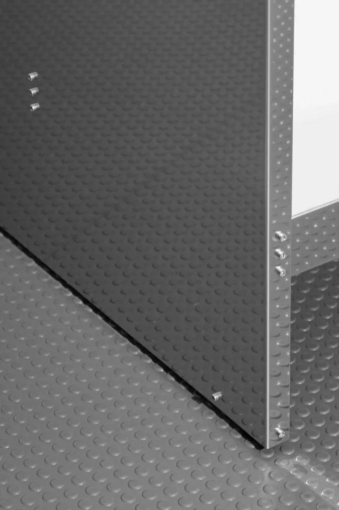 Close-up of a dark textured metal panel joined to a reflective perforated metal frame with exposed bolts