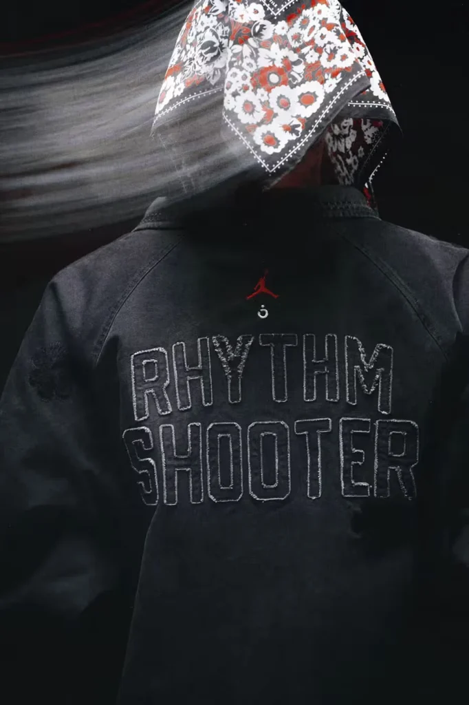 Back view of a person in a black jacket reading “RHYTHM SHOOTER,” with a red Jordan logo and floral bandana hood against a