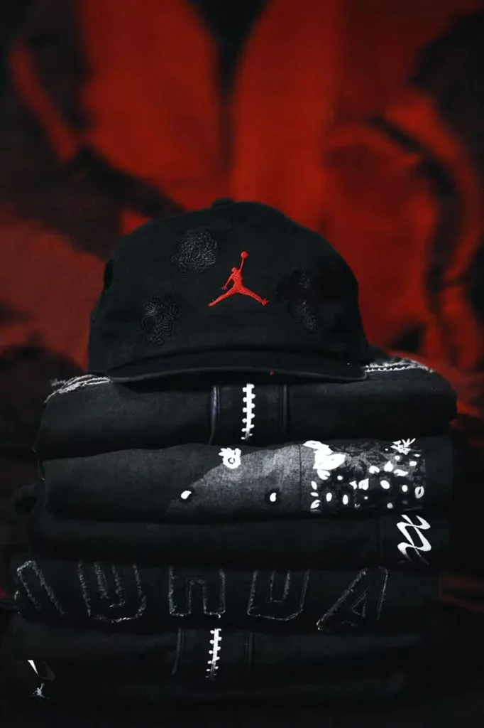 Stacked black baseball caps and garments with red Jumpman logos, white stitching, and floral graphics against a red backdrop