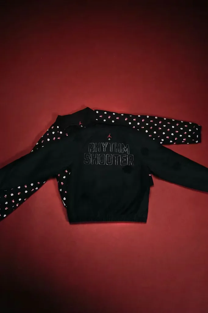 Black jacket with floral-patterned sleeves and “RHYTHM SHOOTER” text, laid flat on a red background
