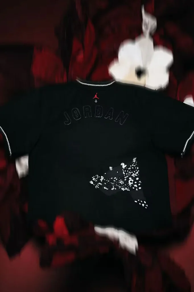 Black Jordan sweatshirt with red Jumpman logo, outlined “JORDAN” lettering and white floral graphic, against a blurred red