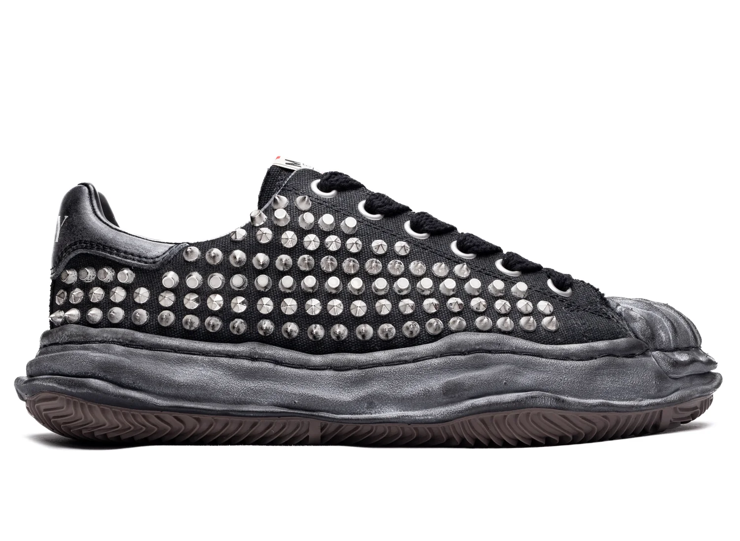 Single black low-top sneaker covered in rows of silver studs, with a thick sculpted black sole on a white background