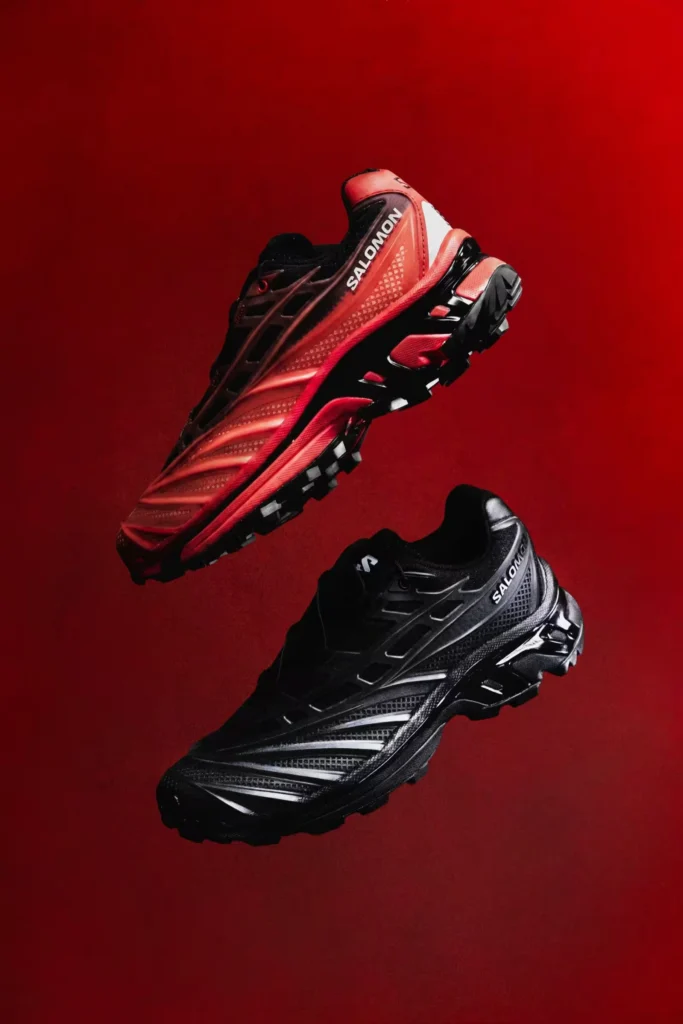 Two Salomon trail shoes, one red and one black, float against a red background, showing rugged lugged soles