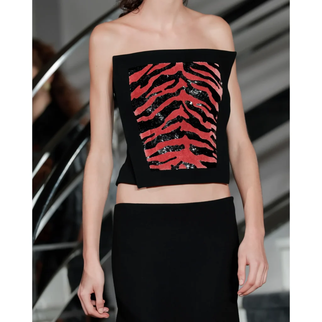 Model in a black strapless crop top with a red-and-black abstract striped panel and matching black skirt beside a curved ramp
