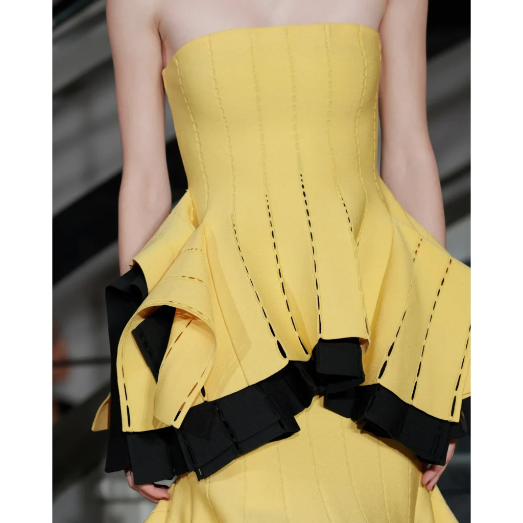 Close-up of a model in a yellow strapless corset dress with black layered ruffles and contrasting stitch details