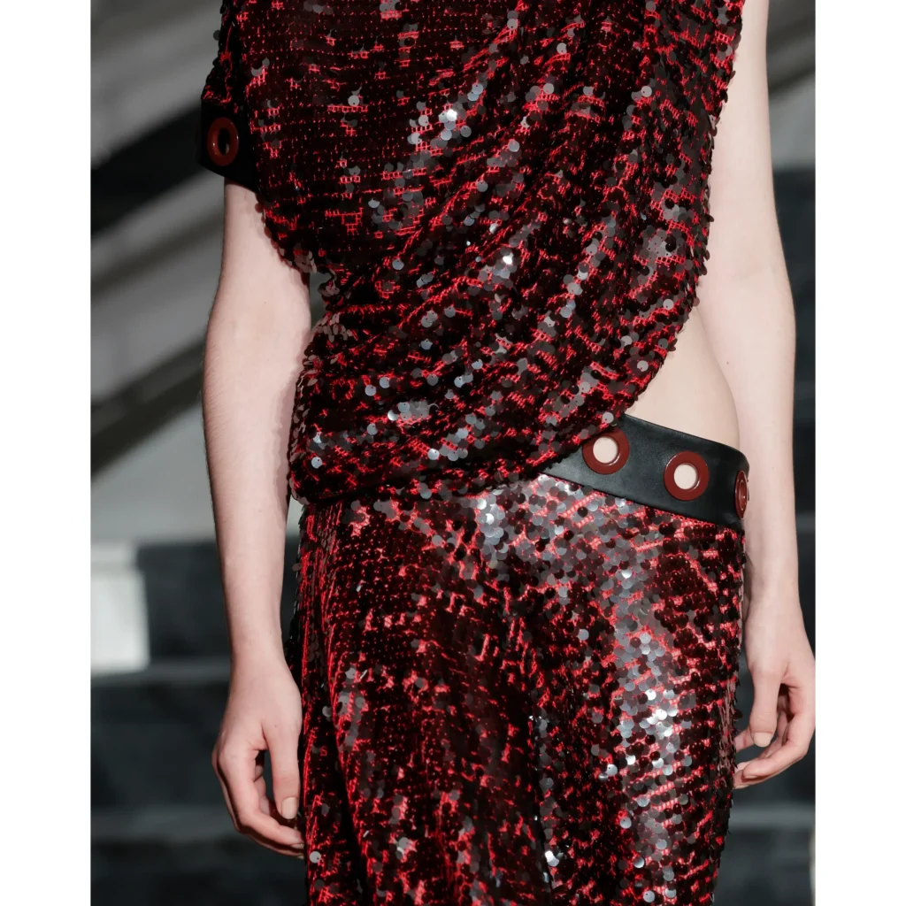 Close-up of a red and black sequined dress with silver accents and a wide black grommet belt