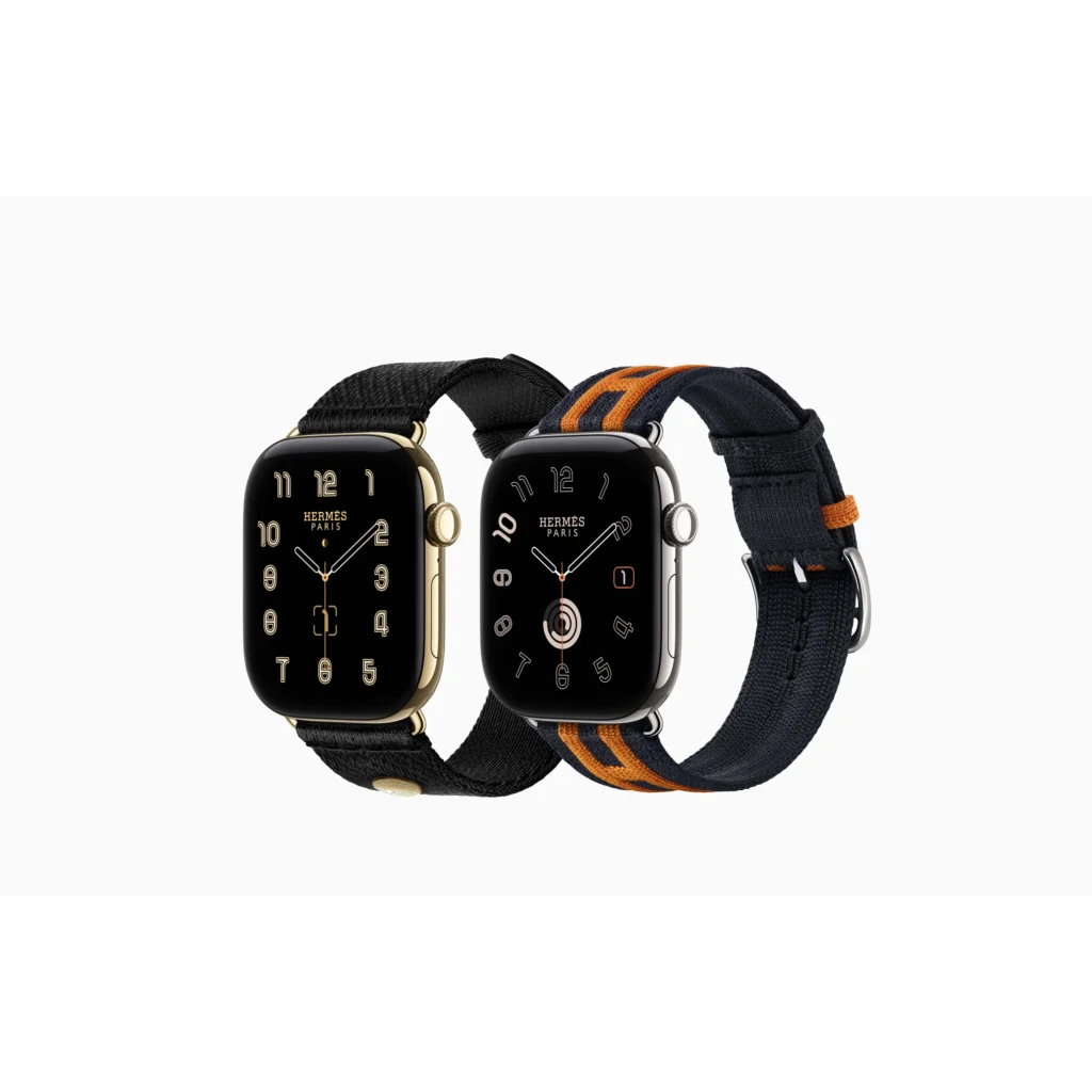 Two Hermès Apple Watches with black faces and textile bands, one black and gold, the other navy with orange stripes, on