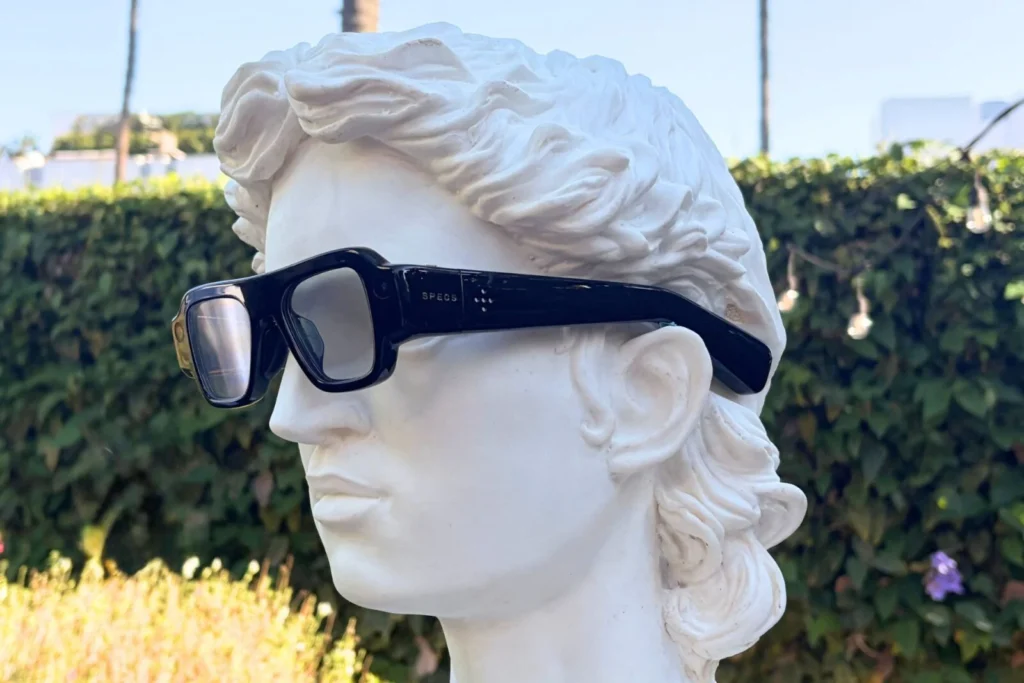 White classical bust wearing oversized black smart glasses in a sunlit garden