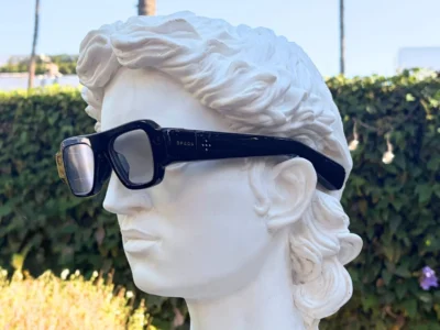 White classical bust wearing oversized black smart glasses in a sunlit garden
