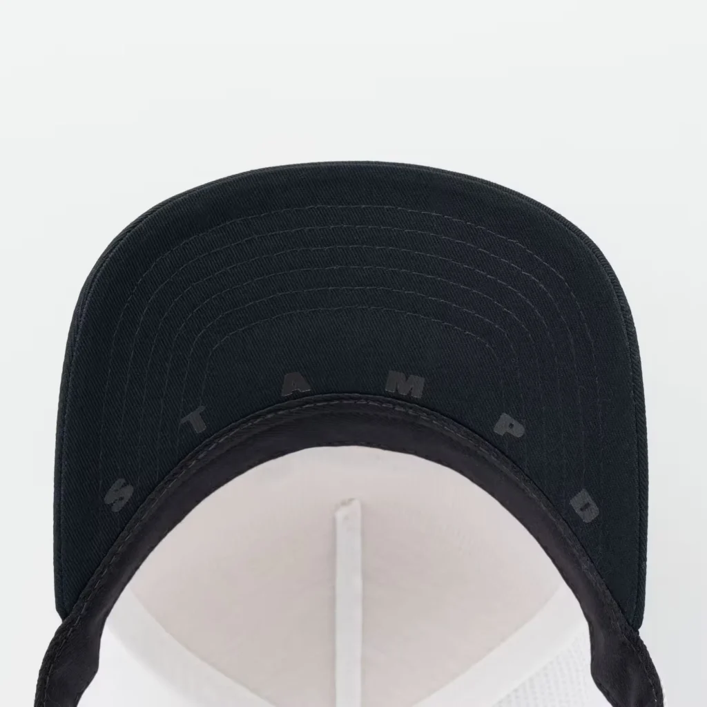Close-up of a black twill trucker cap showing tonal stitched lettering and curved brim against a white background