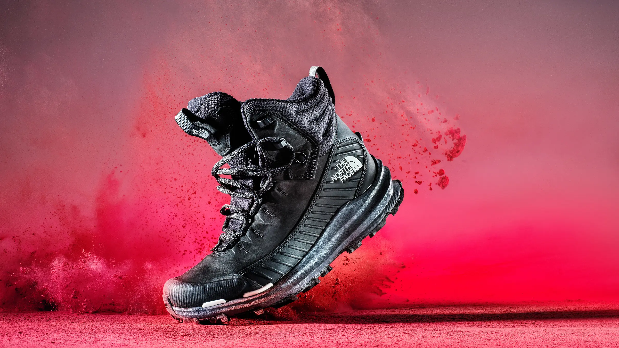 Black hiking boot suspended above a surface against a red, powder-filled background