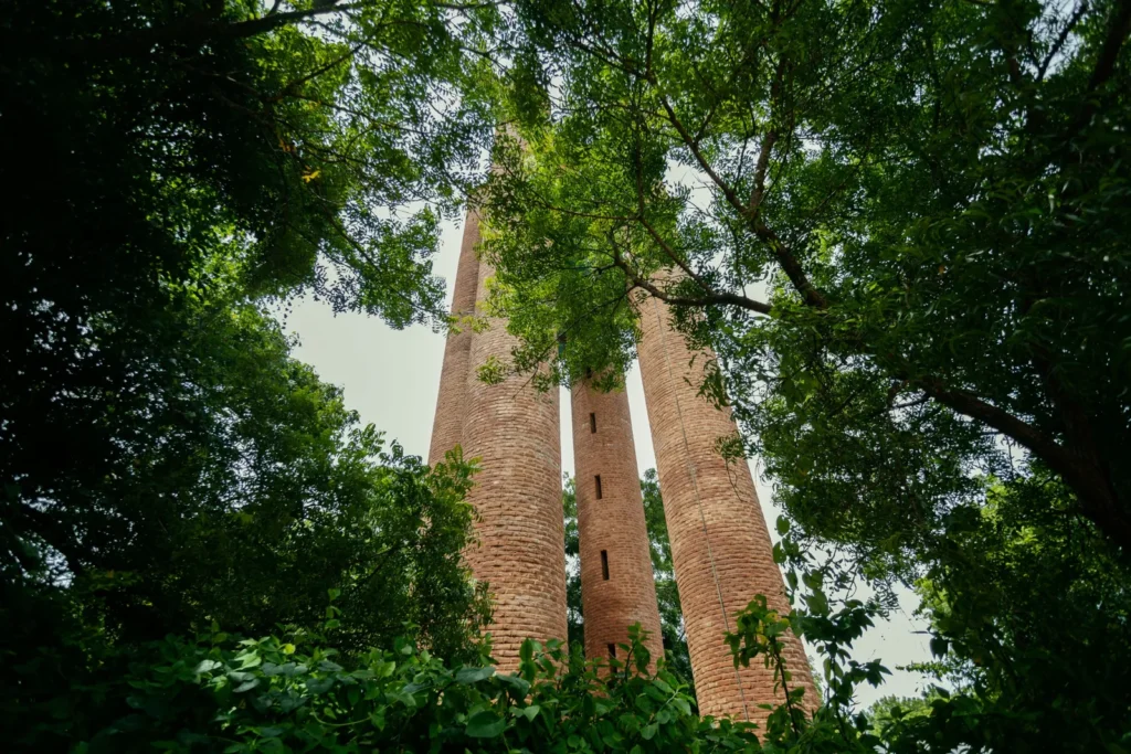 Three tall cylindrical brick towers rise amid dense green foliage, viewed from below through the tree canopy