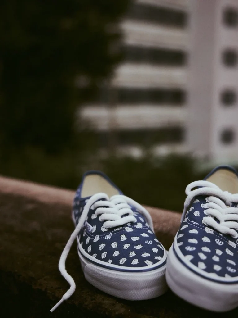 Pair of navy canvas sneakers with white patterned prints, laces, and rubber soles on a ledge outdoors