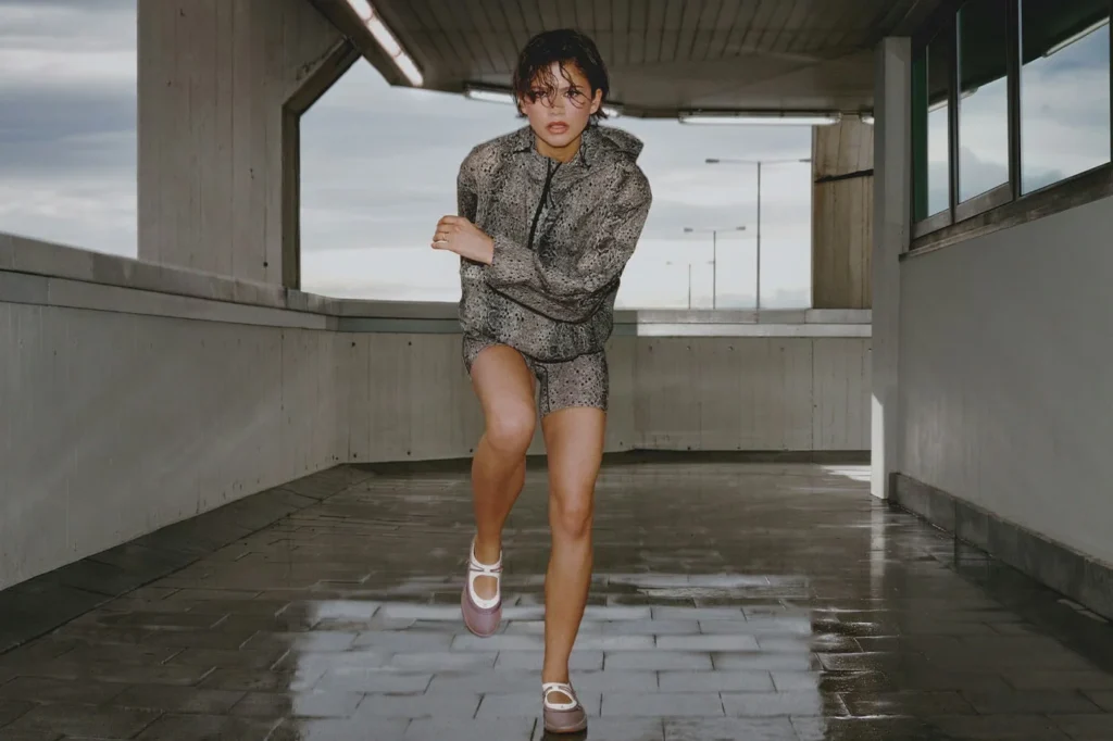 Zendaya strides toward the camera in a gray snakeskin hoodie and shorts with platform Mary Jane shoes on a wet walkway