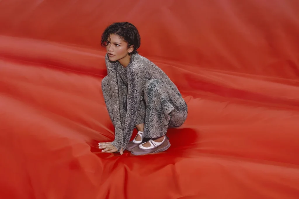 Zendaya crouches on a rippled red surface in a snakeskin-print outfit and mauve Mary Jane shoes