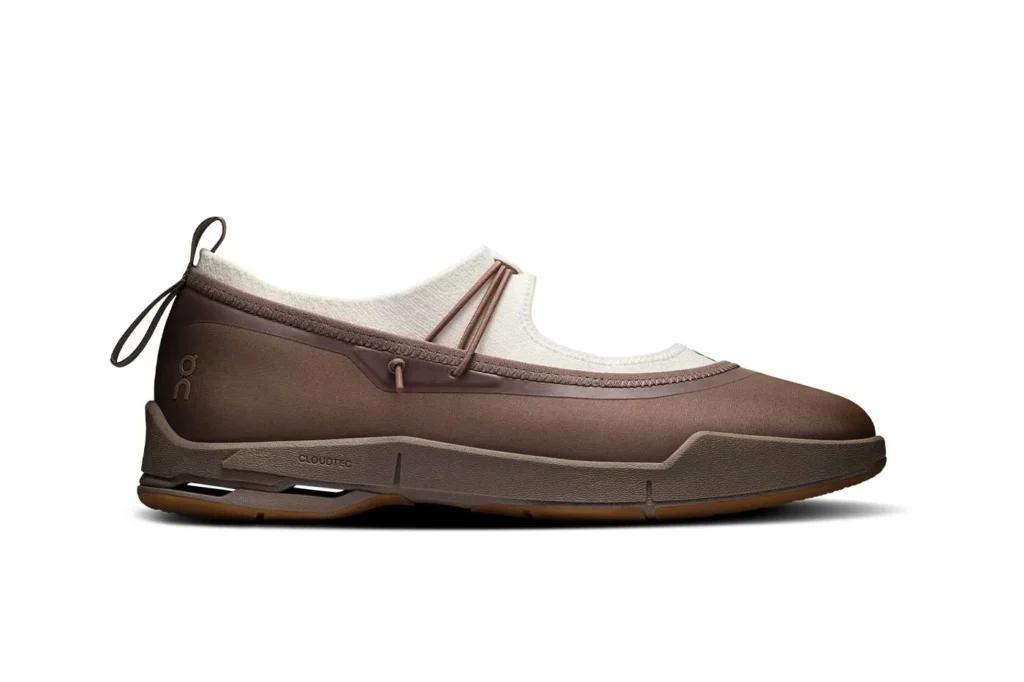 Side view of a brown On slip-on sneaker with cream lining, looped laces, textured sole, and gum outsole on white background