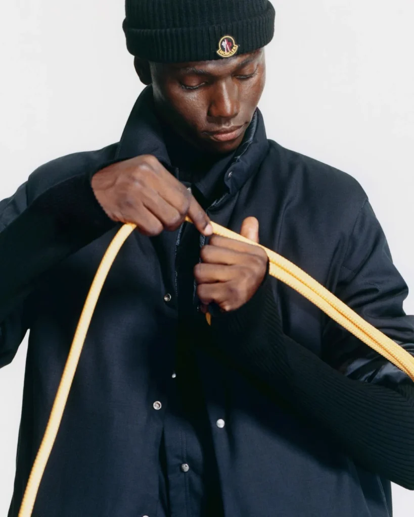 Man wearing a black beanie and jacket adjusts a bright yellow drawstring against a plain white background