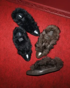 Four furry slippers—two black and two brown—arranged on a red carpet-patterned surface