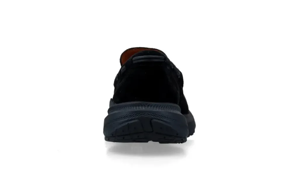 Rear view of a black suede loafer with a thick textured sole on a white background