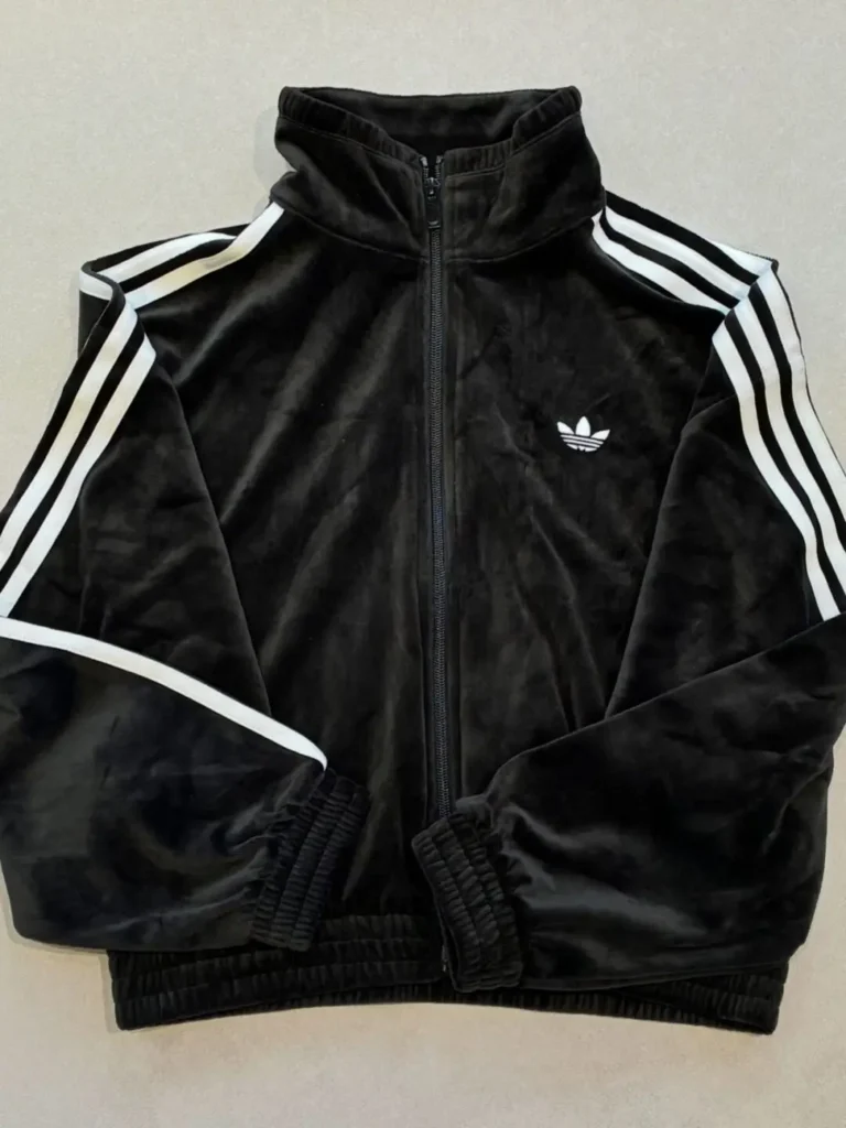 Black Adidas track jacket with white stripes and trefoil logo laid flat against a light background