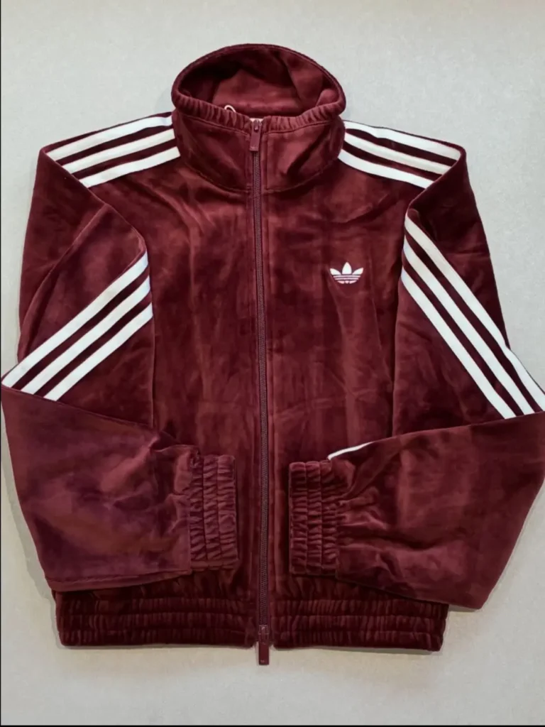 Maroon Adidas track jacket with white triple stripes on shoulders and sleeves, zipped front, and stand-up collar