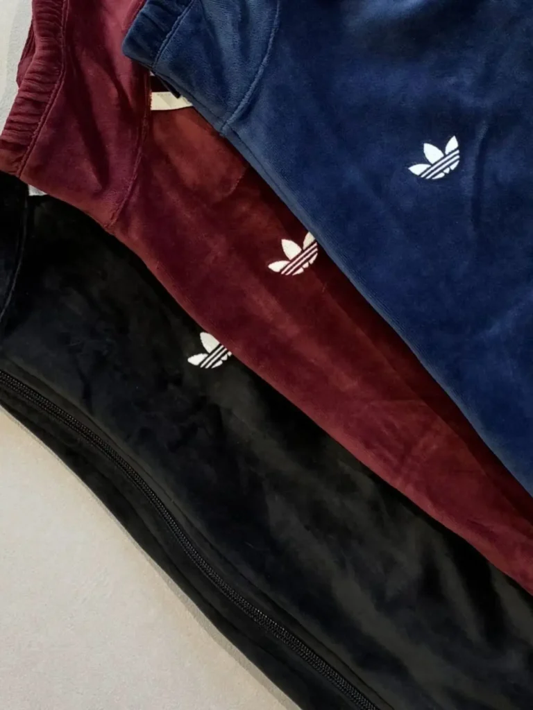 Blue, burgundy, and black Adidas garments layered diagonally, each featuring a white trefoil logo