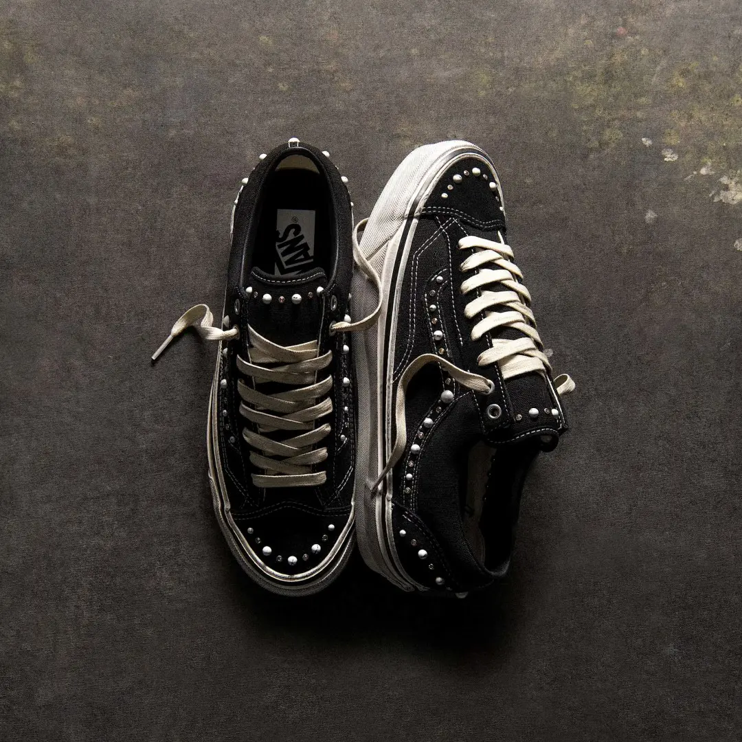 Pair of black Vans Old Skool sneakers with white laces, soles and pearl-like studs on a dark textured surface