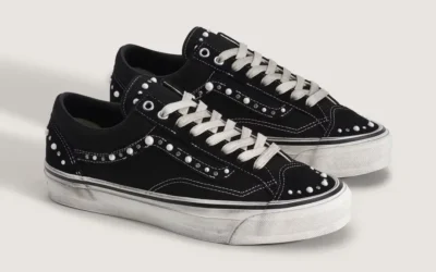 Pair of black low-top sneakers with white laces, contrast stitching, studded panels and white rubber soles on a light