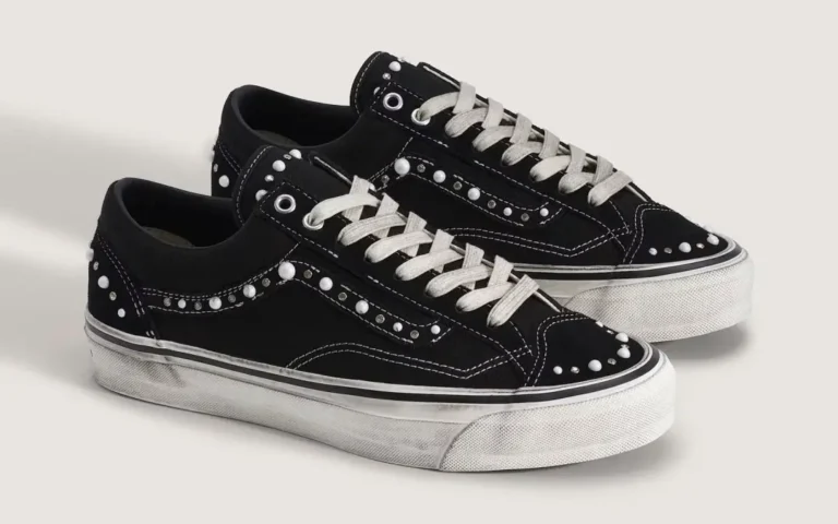 Pair of black low-top sneakers with white laces, contrast stitching, studded panels and white rubber soles on a light