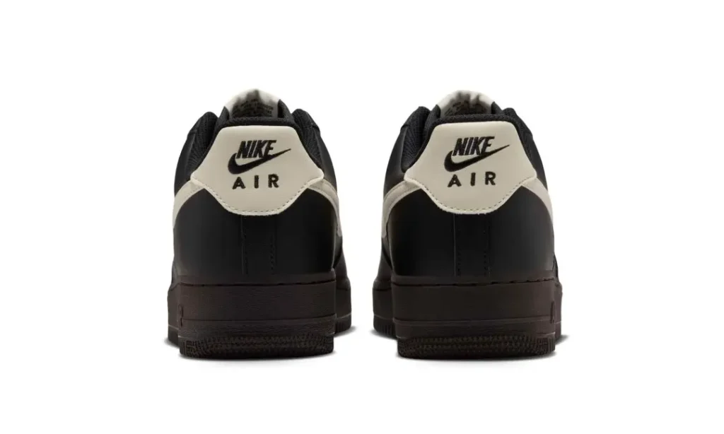 Rear view of black Nike Air sneakers with cream heel panels and logos, standing side by side on a white background