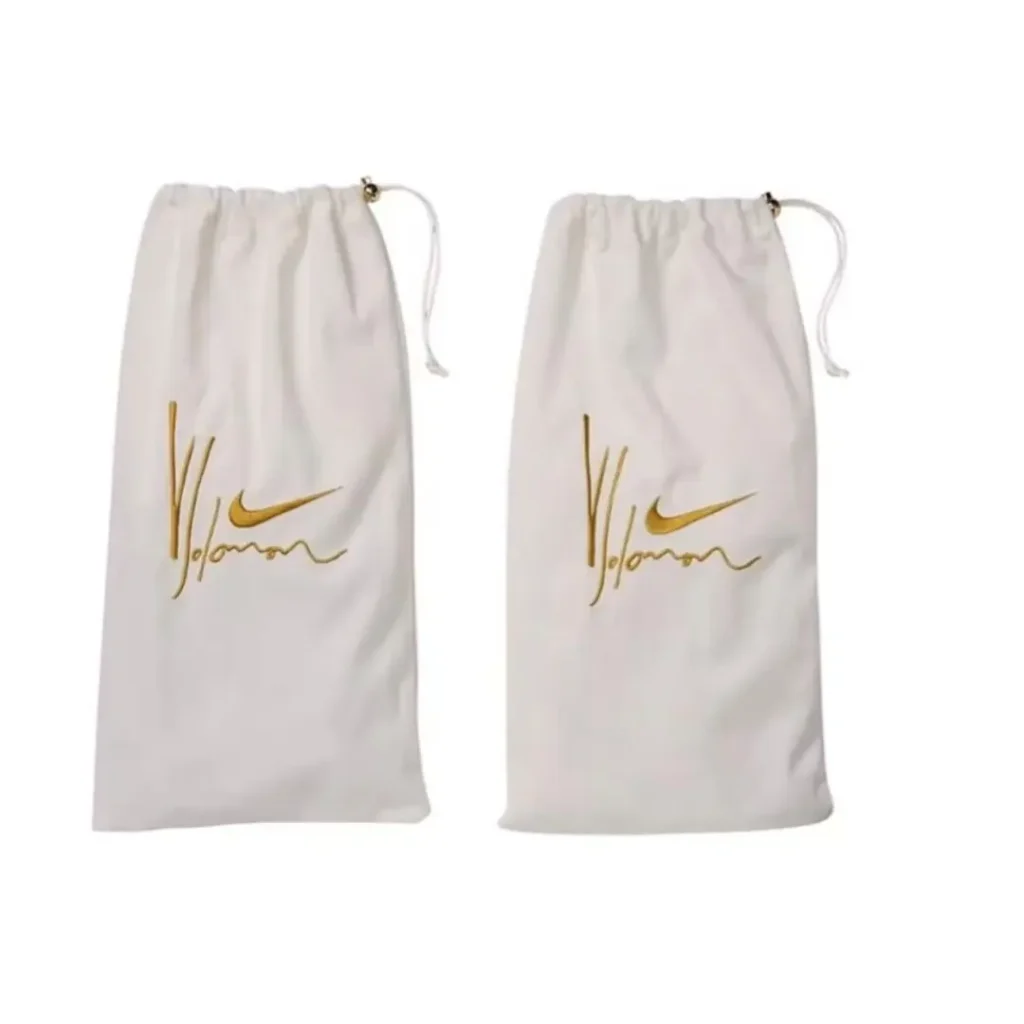 Two white drawstring shoe bags with gold Nike swooshes and cursive lettering, arranged side by side on white background
