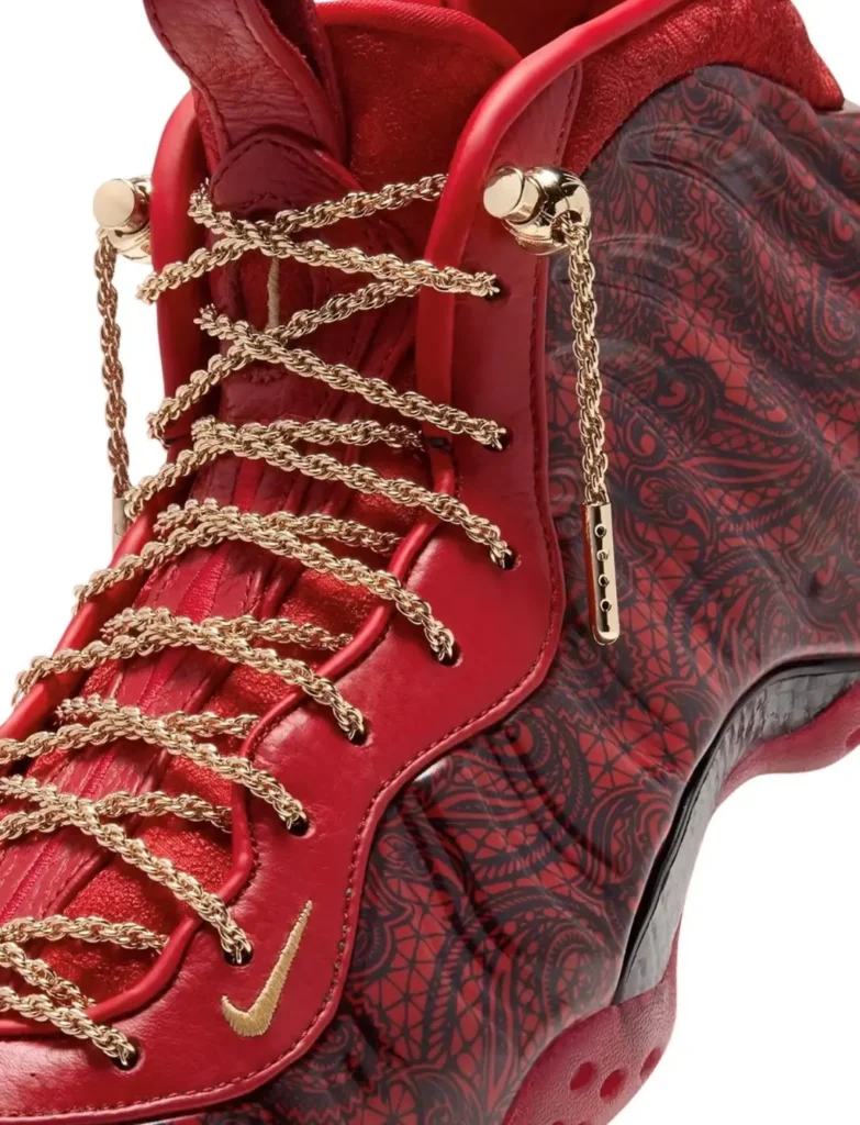 Close-up of a red Nike high-top shoe with gold chain laces and a dark patterned side panel