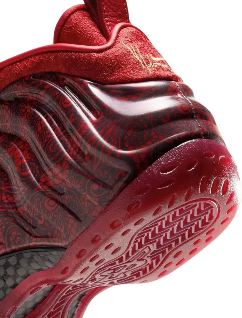 Close-up of a red sneaker with glossy black-and-red patterned panels and a textured red rubber sole against white background