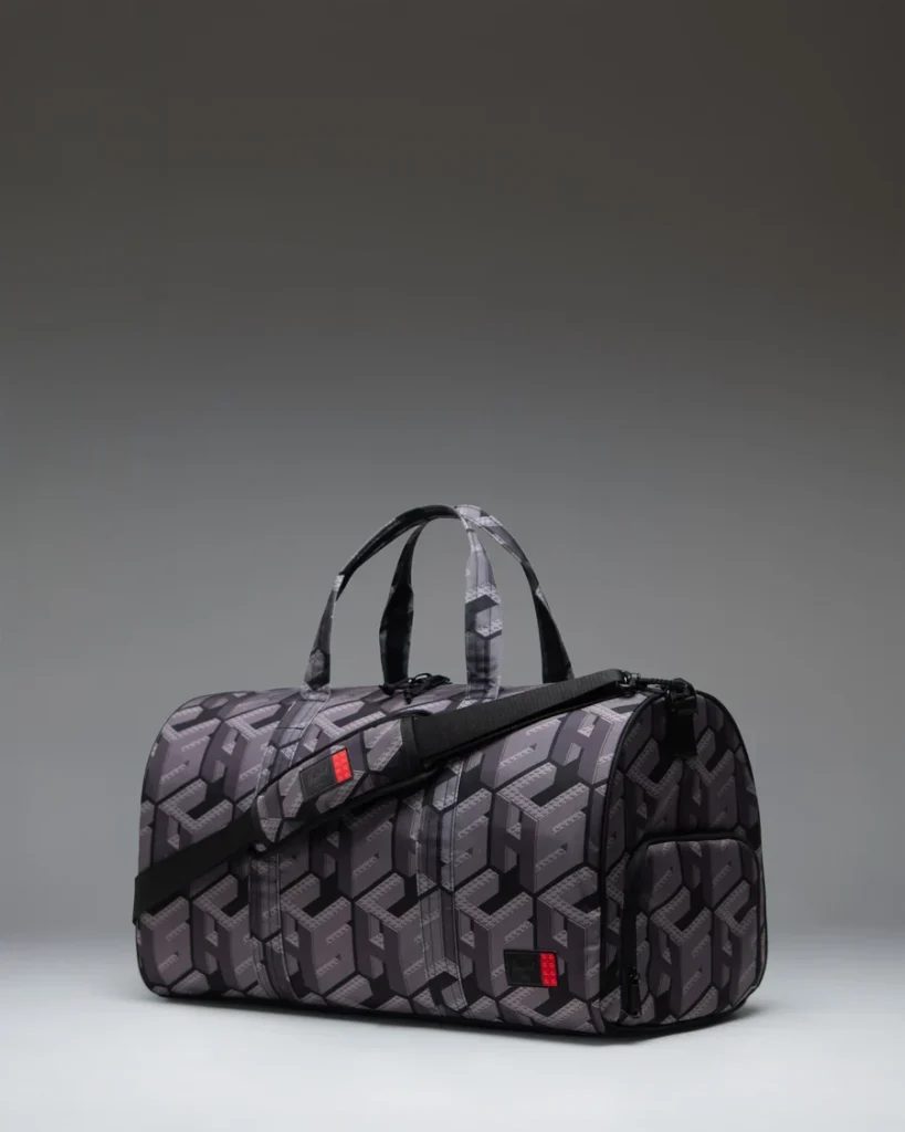 Black and gray patterned duffel bag with handles, shoulder strap, and zippered side pocket against a gray background