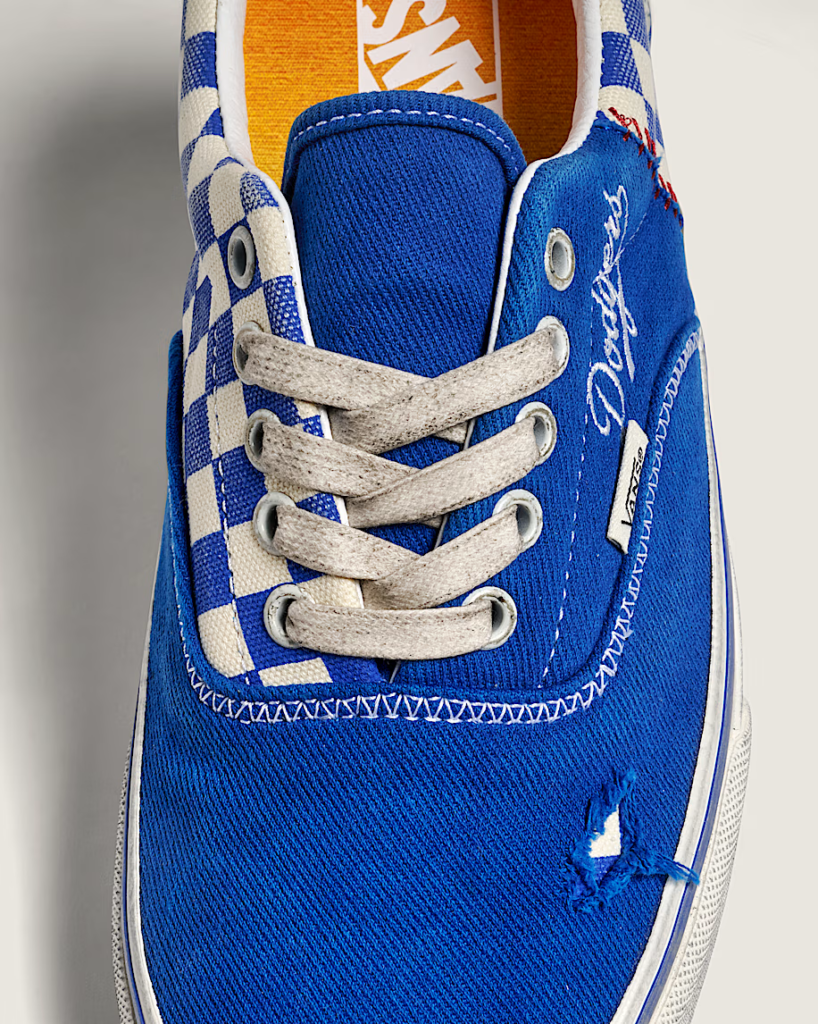 Close-up of a blue-and-white Vans sneaker with checkerboard panels, gray laces, and Dodgers script on the side