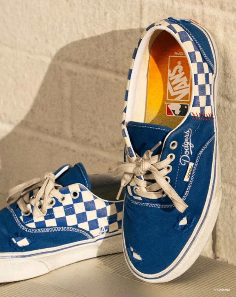 Pair of blue Vans sneakers with white checkerboard panels, Dodgers script, MLB logo and cream laces on a beige surface