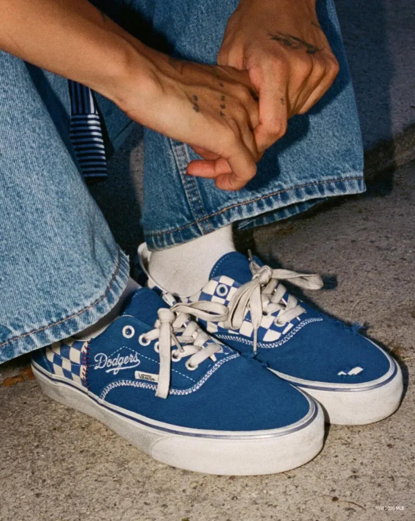 Close-up of blue Dodgers Vans sneakers with white laces, worn with cuffed jeans on concrete