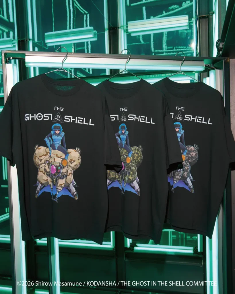 Three black T-shirts display Ghost in the Shell graphics on hangers against glowing green fluorescent lights