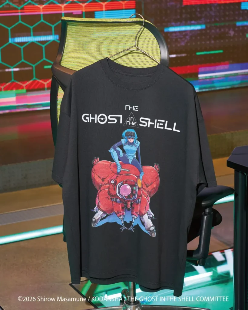 Black T-shirt on a hanger featuring a blue-haired character riding a red mechanical spider, displayed before a neon screen