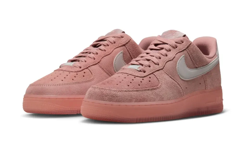 Pair of dusty pink Nike low-top sneakers with suede uppers, white swooshes and matching rubber soles on white background