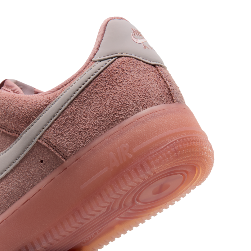 Close-up of a dusty pink Nike sneaker with suede panels, gray swoosh, and translucent gum sole against a white background