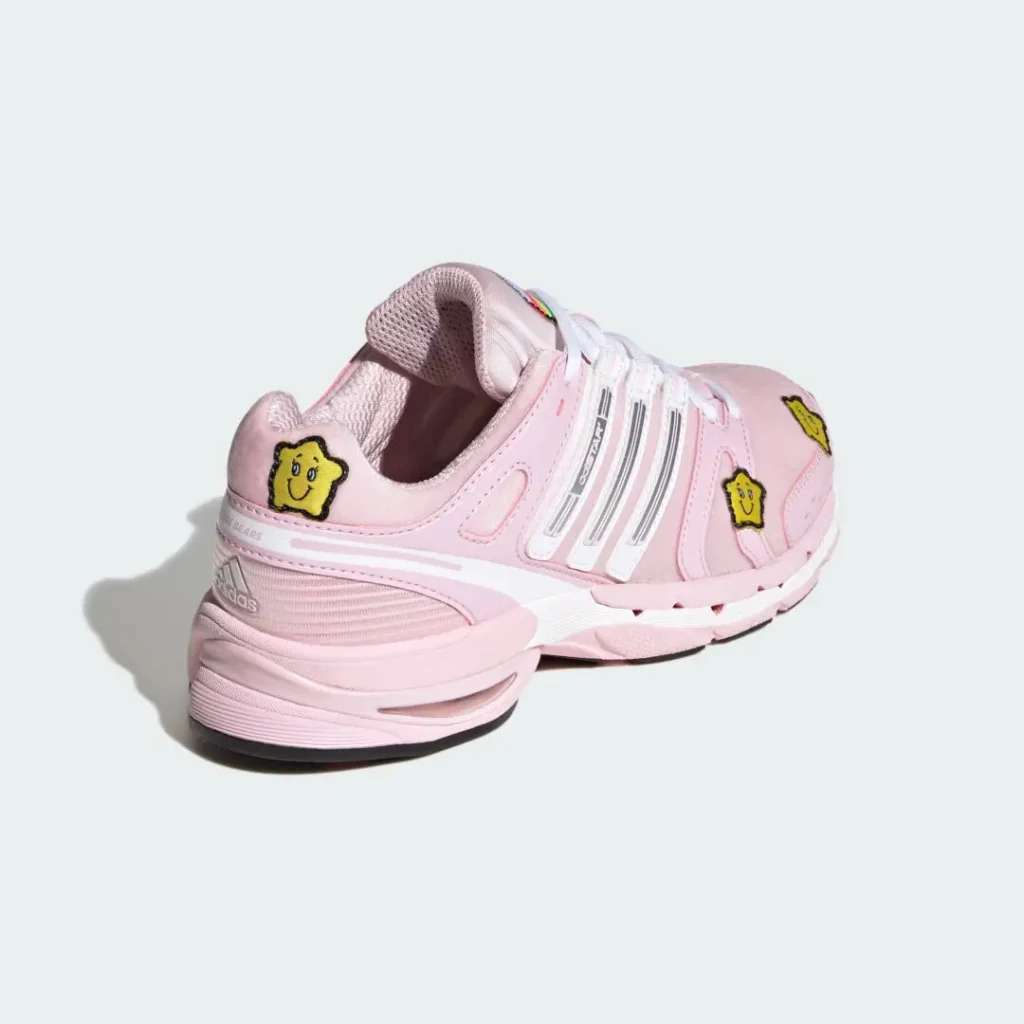 Pair of pink Adidas sneakers with white stripes and yellow smiling flower patches on a pale background