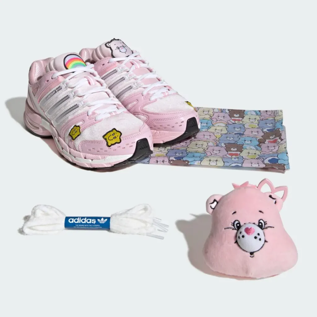 Pink character-themed sneakers, patterned fabric, white Adidas laces, and a pink plush toy arranged on a pale background
