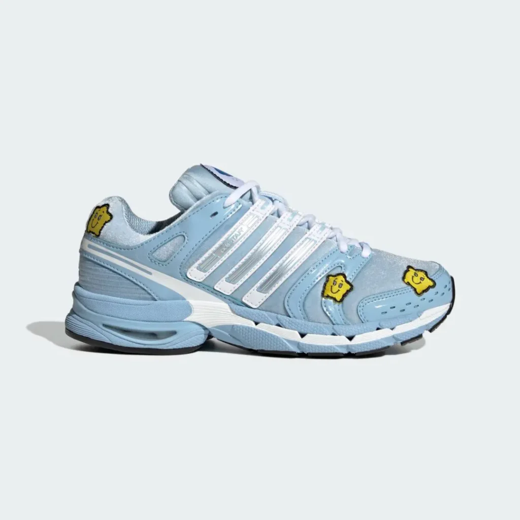 Light blue and silver sneaker with white stripes, yellow cartoon patches, and a chunky sole on a pale background