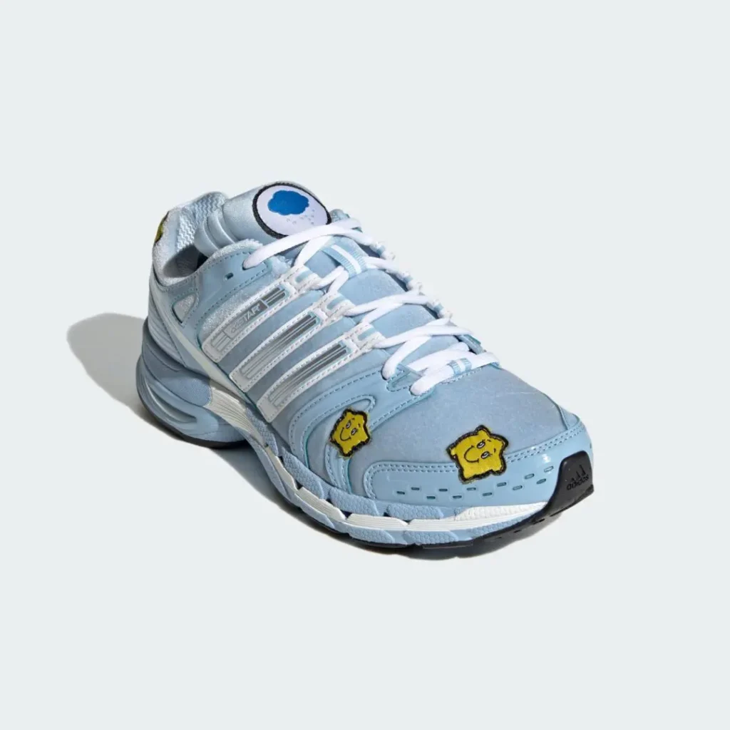 Light blue Adidas sneaker with white laces, gray stripes, and two yellow cartoon patches on the toe box