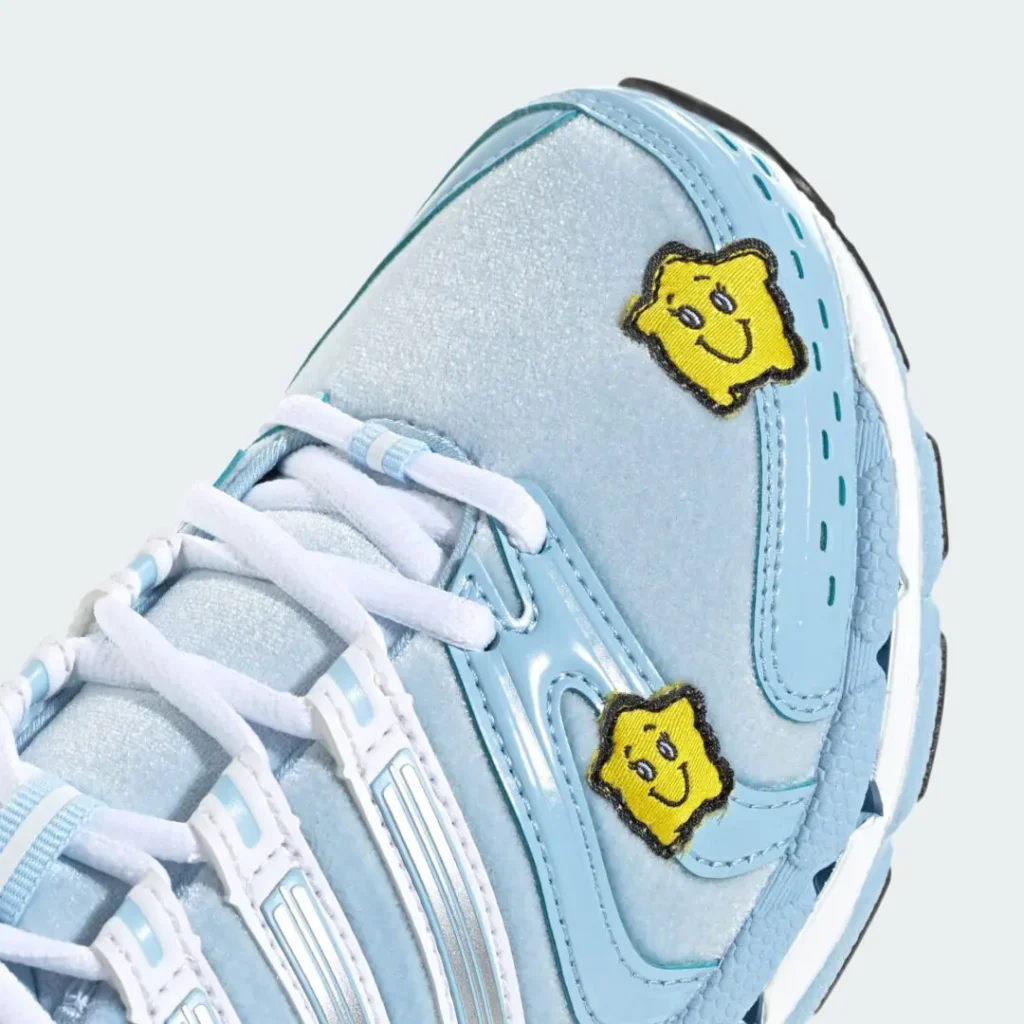 Close-up of a light blue sneaker with white laces and two yellow smiling flower patches, isolated against a pale background