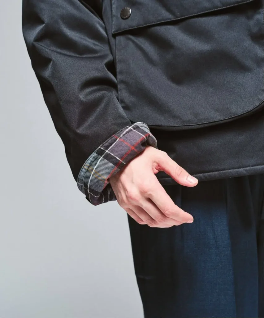 Close-up of a person in a dark jacket with a red, white, and gray plaid cuff and hand extended downward