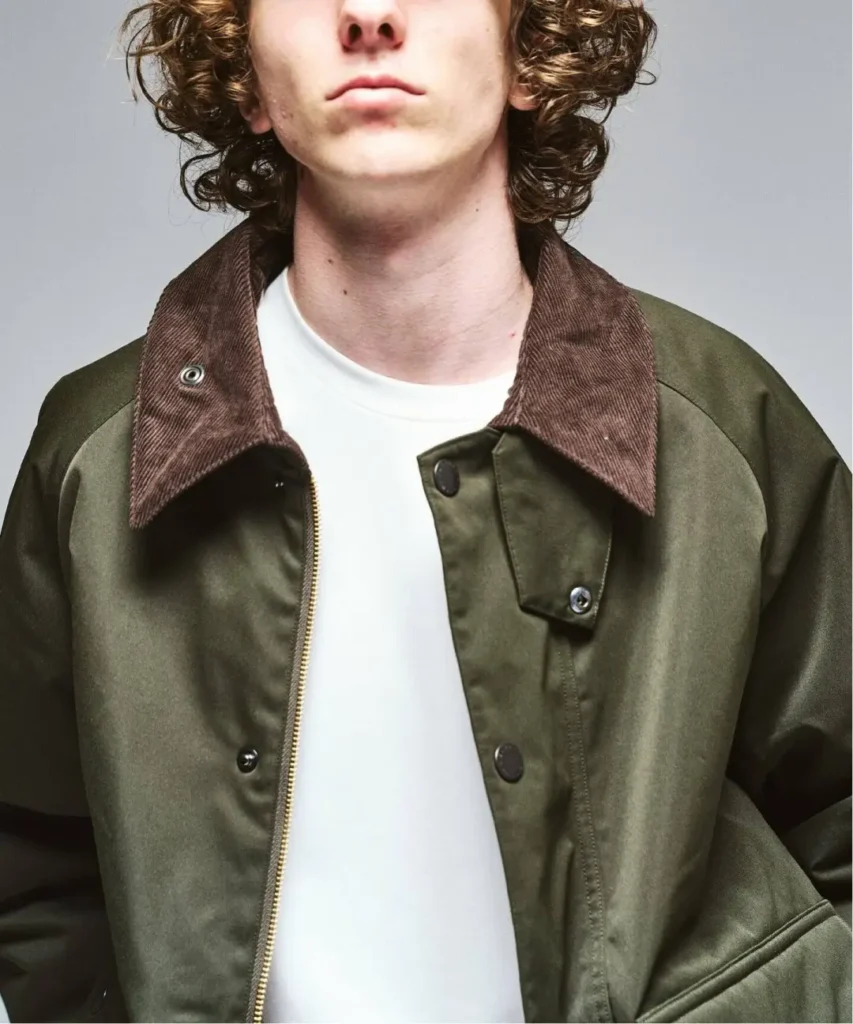 Close-up of a curly-haired person wearing an olive jacket with a brown corduroy collar over a white shirt