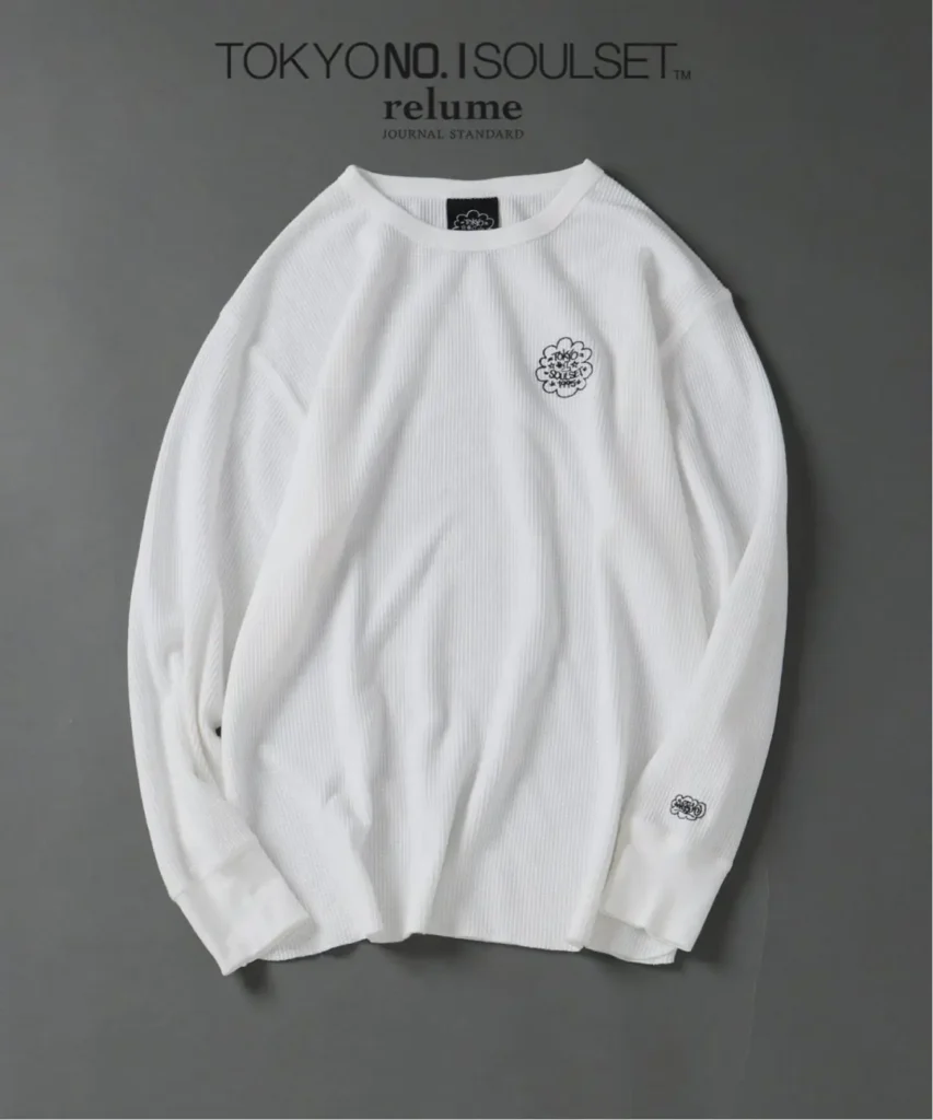 White ribbed long-sleeve shirt laid flat on a gray background, with small black chest and sleeve logos